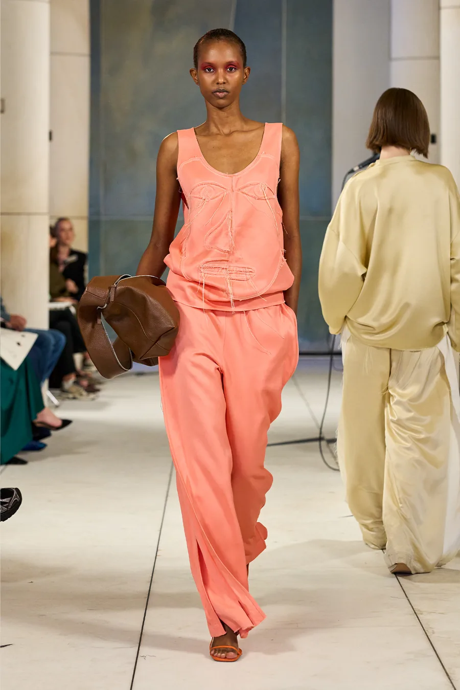 SHOWstudio, Litkovska S/S 27 STRICHA: model in a coral top and wide coral trousers carrying a brown leather bag